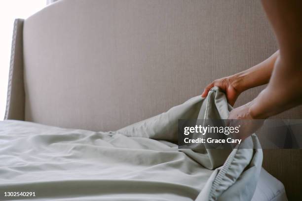 woman puts sheet on bed - bedding foto e immagini stock