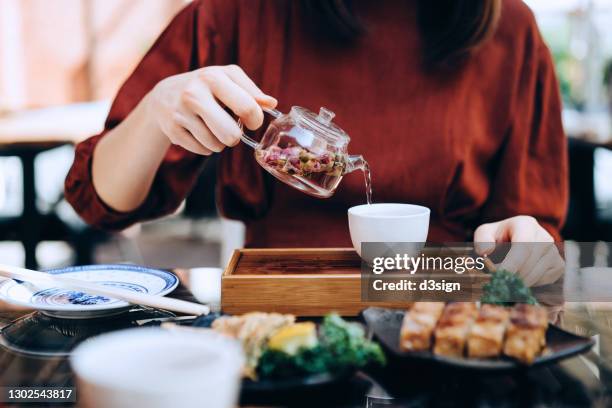 close up of asian woman enjoying assorted freshly served traditional dim sum in outdoor chinese restaurant. she is holding a transparent teapot and pouring rose bud tea in cup on dining table. traditional chinese culture, yumcha, eating out lifestyle - hong kong food stock-fotos und bilder