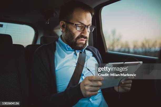 hombre de negocios usando tablet pc en el coche. foto de un hombre de negocios sentado en el asiento trasero de una limusina de pasajeros - un viaje de negocios - firma digital fotografías e imágenes de stock