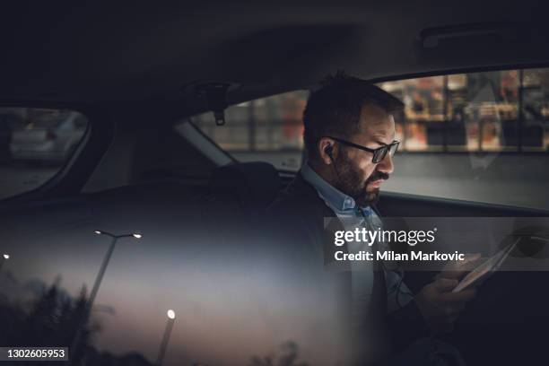 hombre de negocios usando tablet pc en el coche. foto de un hombre de negocios sentado en el asiento trasero de una limusina de pasajeros - un viaje de negocios - firma digital fotografías e imágenes de stock