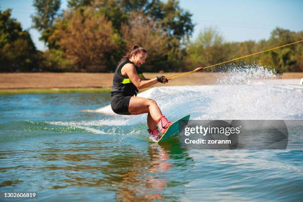 smiling young woman tilting wakeboard upwards and spraying - waterskiing stock pictures, royalty-free photos & images