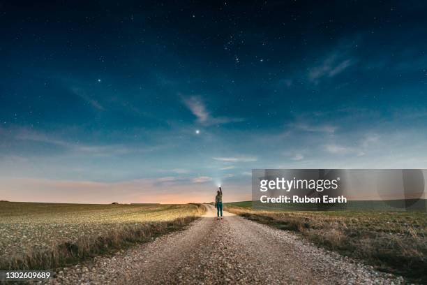 woman pointing a lantern to the sky while walking on a country road at night with the clear sky full of stars - dusk stock pictures, royalty-free photos & images