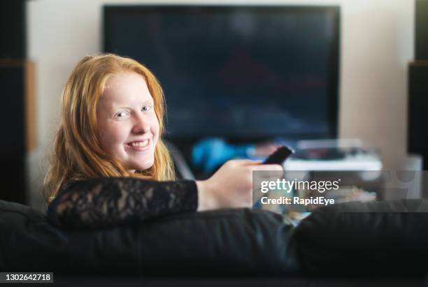 schöne rothaarige junge frau sitzt auf dem sofa vor dem fernseher, halten fernbedienung - pale complexion stock-fotos und bilder