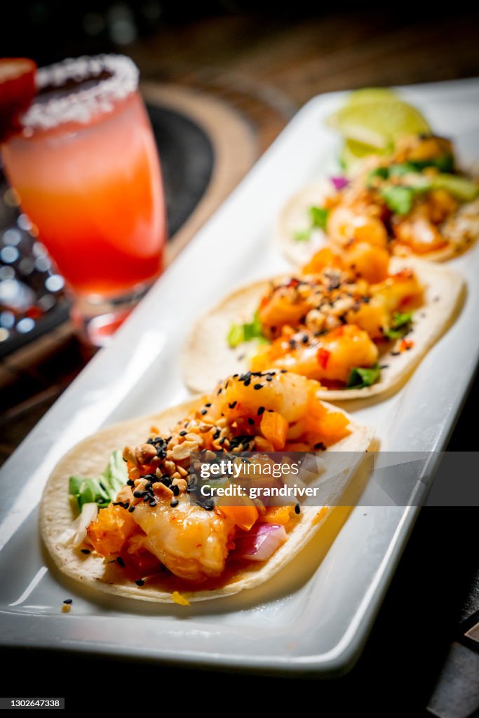 A Platter With Three Gourmet Shrimp Tacos With Mango Habanero Salsa, Strawberry Margarita, Propane Fire Pit In The Background