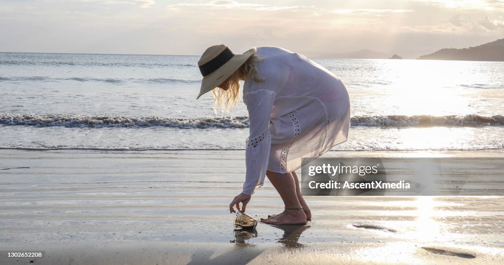 Woman picks up garbage on beach in the morning