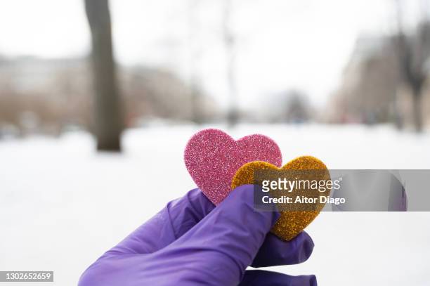 unrecognisable person with rubber surgical gloves holds two heart shapes in a snowy street in the city. berlin, germany. - frostbite fingers stock-fotos und bilder