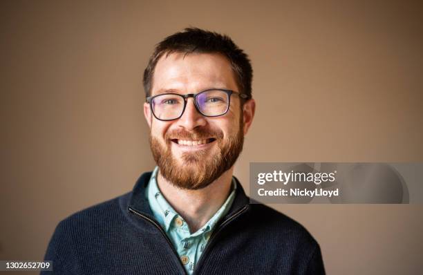 young man with glasses smiling while standing against a brown background - man expressive background glasses stock pictures, royalty-free photos & images