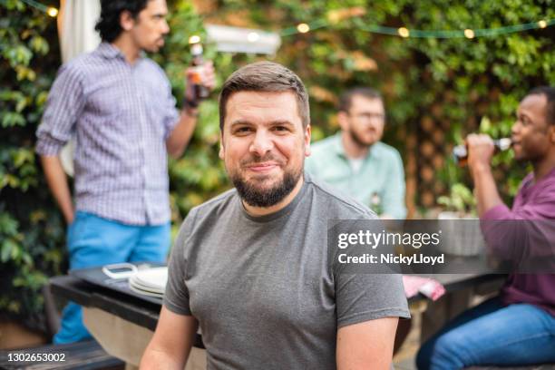 lächelnder junger mann sitzt draußen mit freunden im hintergrund - nur junge männer stock-fotos und bilder