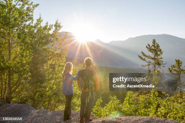 het paar van de wandel bekijkt de zonsondergang over bergen - sun flare couple stockfoto's en -beelden