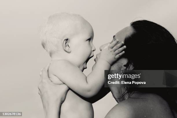 loving mother holding toddler boy, kissing and looking into his eyes - beautiful blonde babes stock pictures, royalty-free photos & images