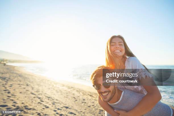 couple playing piggyback on the beach at sunset or sunrise. - andalucia beach stock pictures, royalty-free photos & images