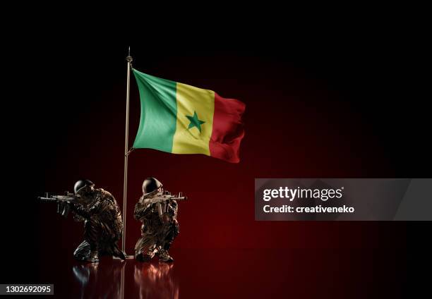 Concept of military conflict with soldier statues and waving national flag of Senegal. Illustration of coup idea. Two guards defending the symbol of country against red wall
