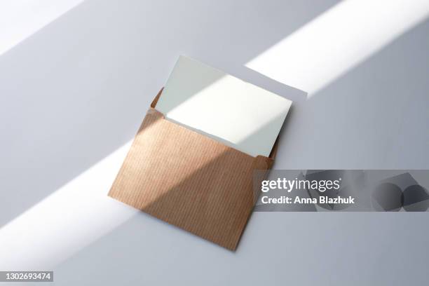 brown envelope with white blank paper card over white background with sunlight and trendy shadows - greeting card and envelope stock pictures, royalty-free photos & images