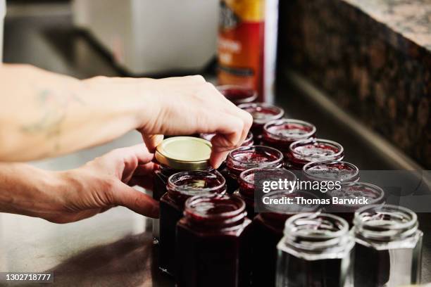 female chef putting lids on jars of freshly made organic jam - jam stock pictures, royalty-free photos & images