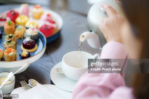 asian women are pouring tea into a glass with cake next to it while eating afternoon tea in a luxury hotel in the afternoon - englische tea time stock-fotos und bilder