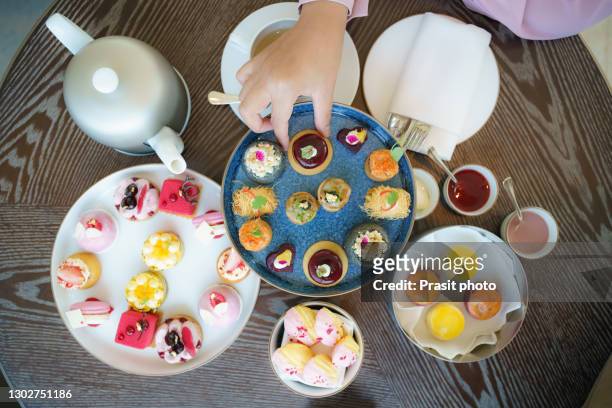 top view of woman hand pick up cake in afternoon tea, cakes and snacks with a teapot in the background. - soirée mousse stock-fotos und bilder