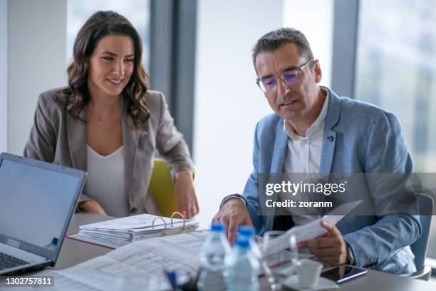 zakenman die financieel rapport analyseert, zijn vrouwelijke collega die en glimlacht kijkt - audit stockfoto's en -beelden