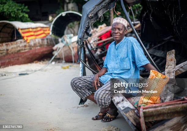 black senior man sitting on coast boat in african village - black market 個照片及圖片檔