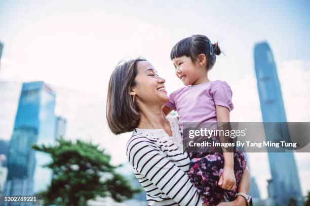 mom holding up and playing with his little daughter joyfully in park in downtown district - toothy smile family outdoors stock pictures, royalty-free photos & images