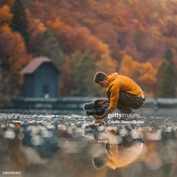 männliche fotograf hält kamera über wasser in der natur - kamerabedienung stock-fotos und bilder