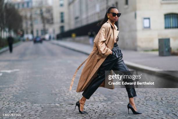 Emilie Joseph wears sunglasses, golden earrings, a beige trench coat from Gestuz, bronze shiny metallic bras as part of a dress from Paco Rabanne,...