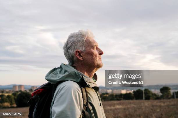 senior male hiker with eyes closed at countryside during sunset - old man close up stockfoto's en -beelden