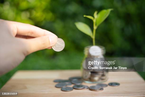 man putting a coins in the jar with plants growing up - crowdfunding stock-fotos und bilder