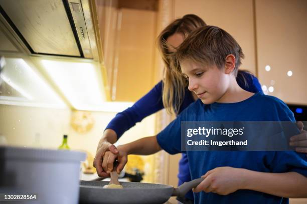 mutter lehrt sohn, wie man crepes in der küche zu machen - pancake toss stock-fotos und bilder