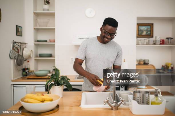 happy african american man washing dishes at home - washing up stock pictures, royalty-free photos & images