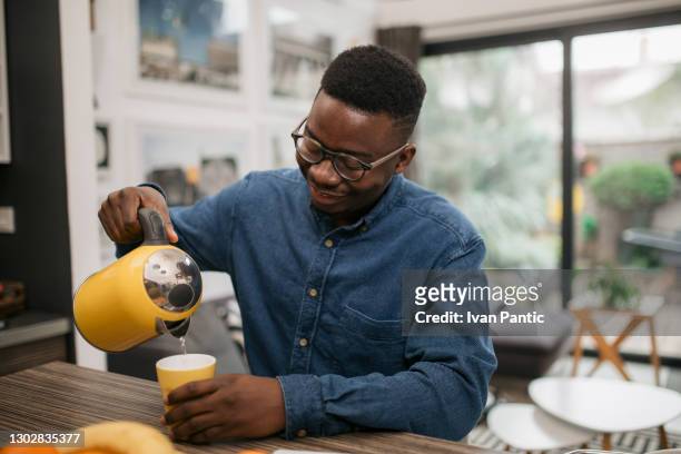 jeune homme afro-américain heureux préparant le thé à la maison - bouilloire photos et images de collection