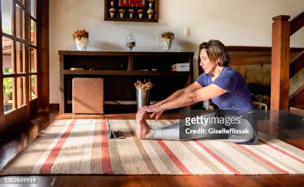 woman stretching at home during a streaming yoga class on a tablet - tocar nos dedos dos pés imagens e fotografias de stock