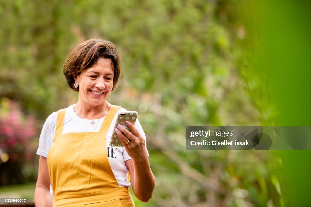 Smiling mature woman video calling on a phone outside in her yard