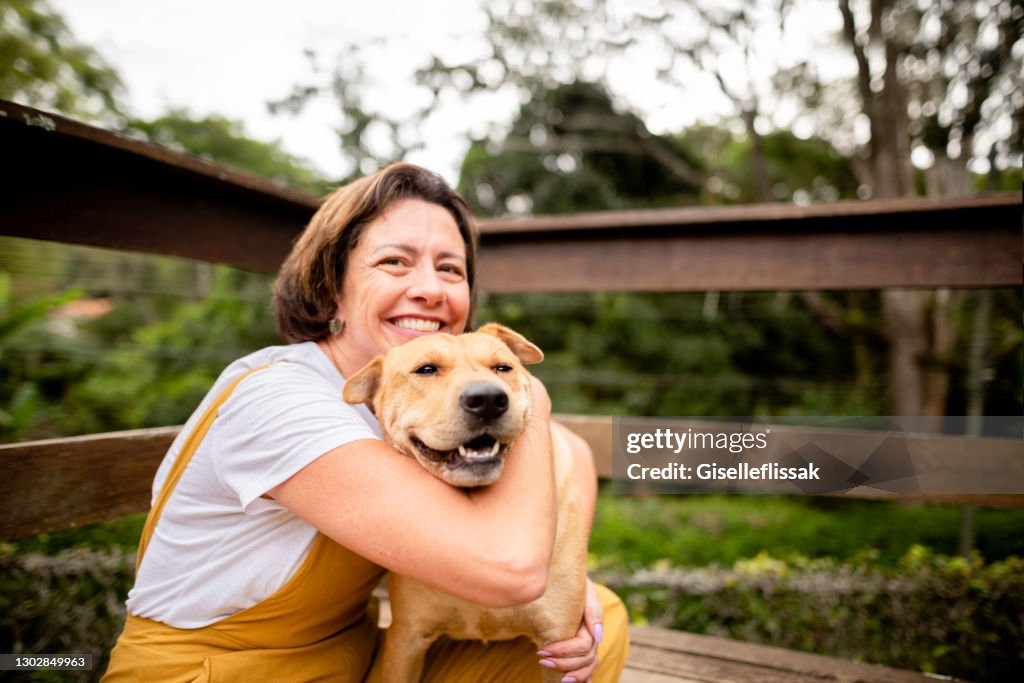 Smiling mature woman hugging her dog outside in her yard