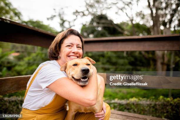 smiling mature woman hugging her dog outside in her yard - average woman stock pictures, royalty-free photos & images