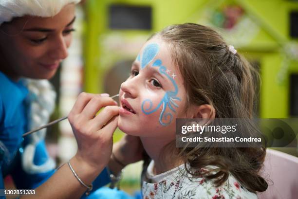 a little girl getting her face painted like a butterfly. - kinder schminken stockfoto's en -beelden