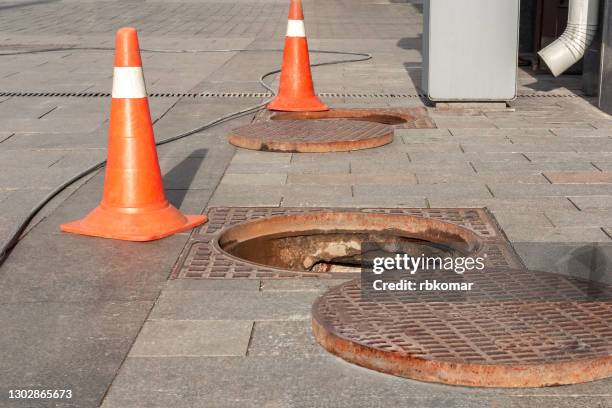 open sewers on the sidewalk of the city and orange bump warning signs. underground work to repairing the accident, urban utility services - マンホール ストックフォトと画像