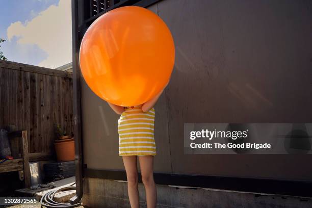 girl holding orange balloon in backyard at home - orange colour stock-fotos und bilder