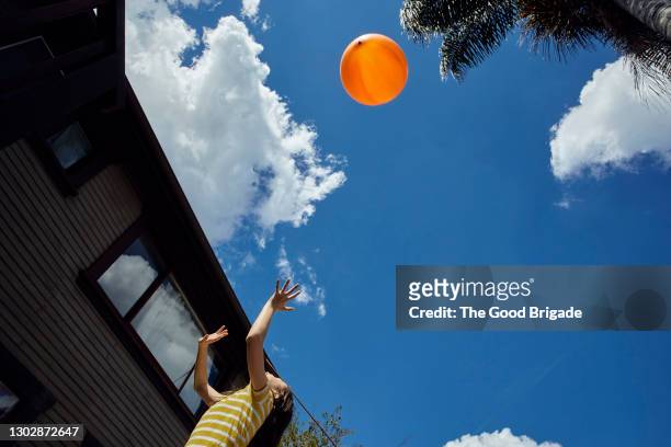girl tossing orange balloon in air against blue sky - orange sky stock-fotos und bilder
