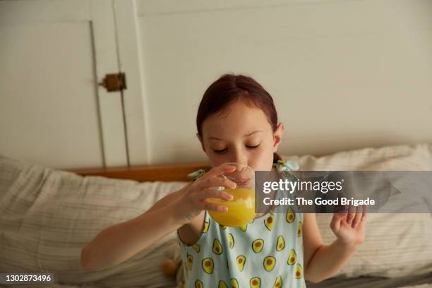 girl drinking orange juice in bed at home - orangensaft stock-fotos und bilder