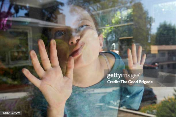 girl pressing face against window at home - pull a face stock-fotos und bilder