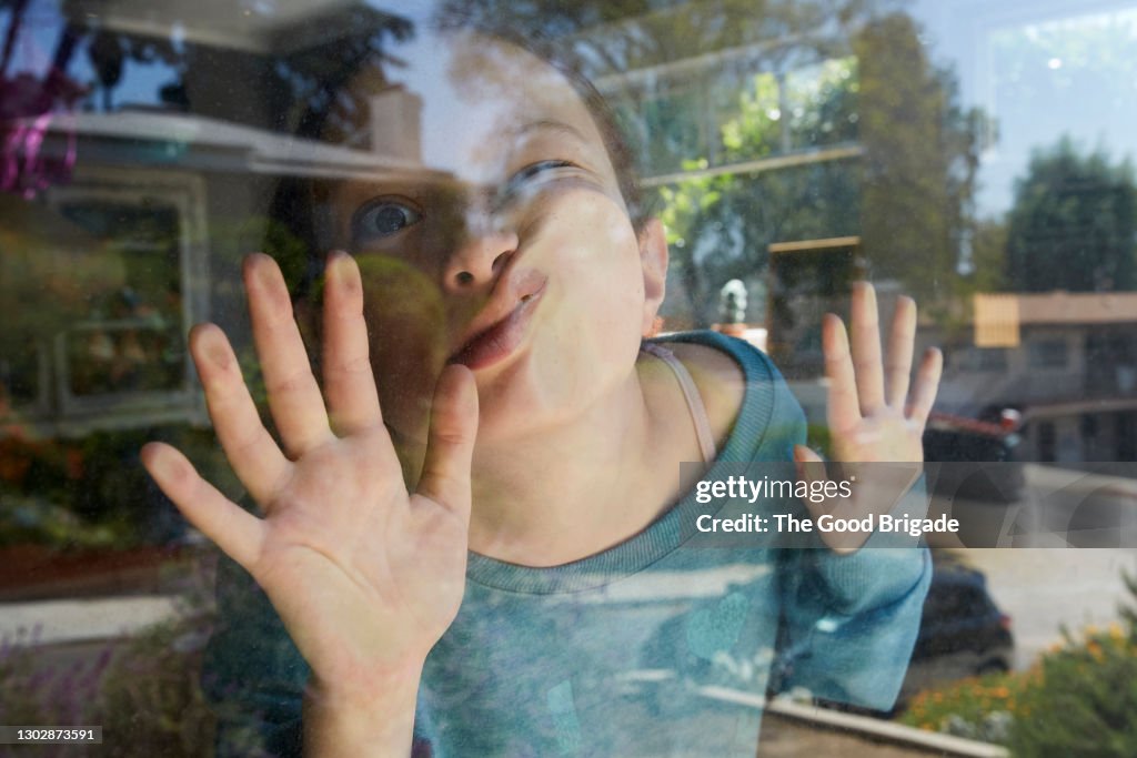 Girl pressing face against window at home