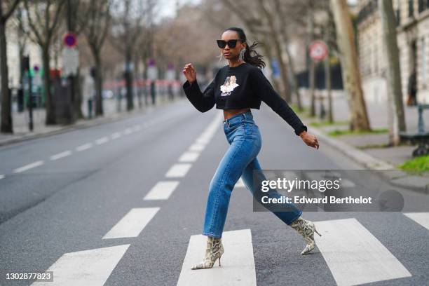 Emilie Joseph wears sunglasses, Isabel Marant bejeweled long earrings, a cropped black pullover with printed angels from Fiorucci, blue ribcage...