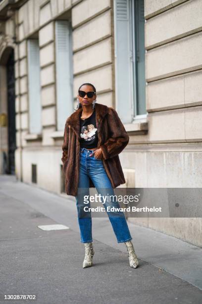 Emilie Joseph wears sunglasses, Isabel Marant bejeweled long earrings, a cropped black pullover with printed angels from Fiorucci, a brown faux fur...