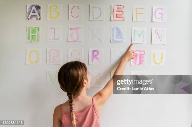 rear view of girl (8-9) looking at alphabet on wall - literate stock-fotos und bilder