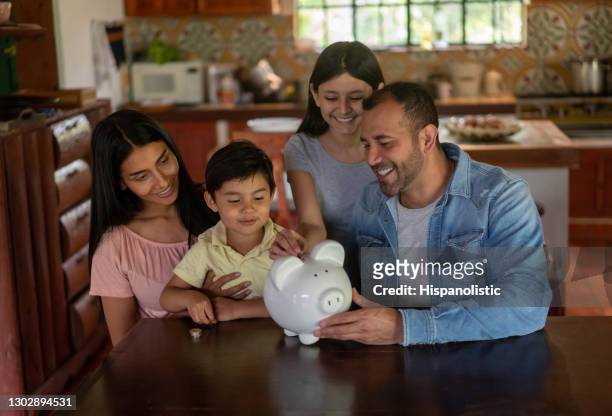 happy latin american family saving money in a piggybank - couple saving piggy bank stock pictures, royalty-free photos & images
