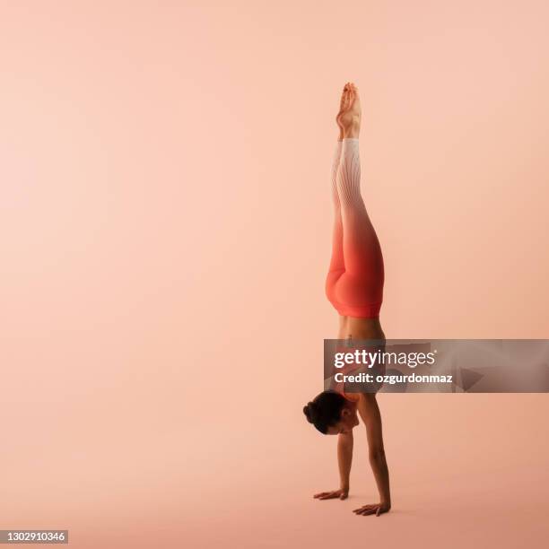 athletische frau trägt sportbekleidung, hose und top, durchführung handstand in yoga - acrobatic yoga stock-fotos und bilder