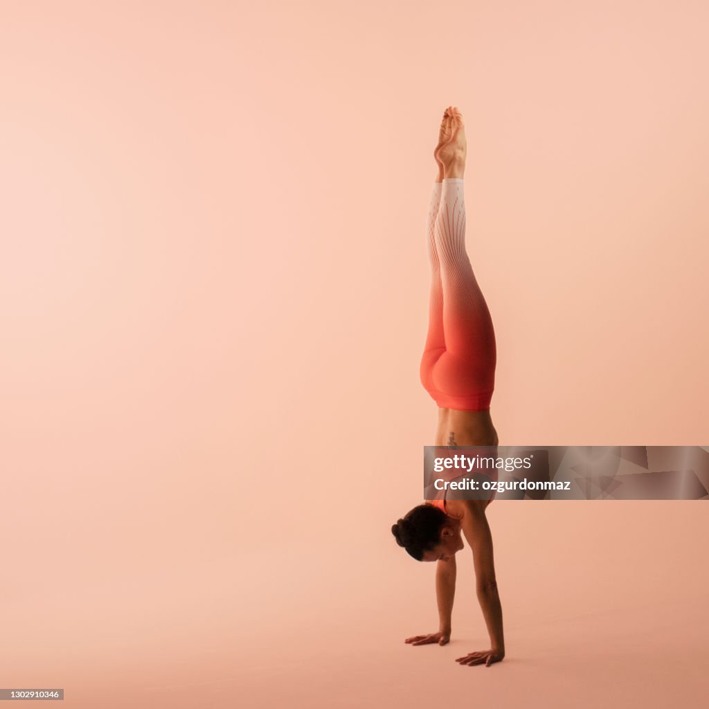 Athletic woman wearing sportswear, pants and top, performing handstand in yoga