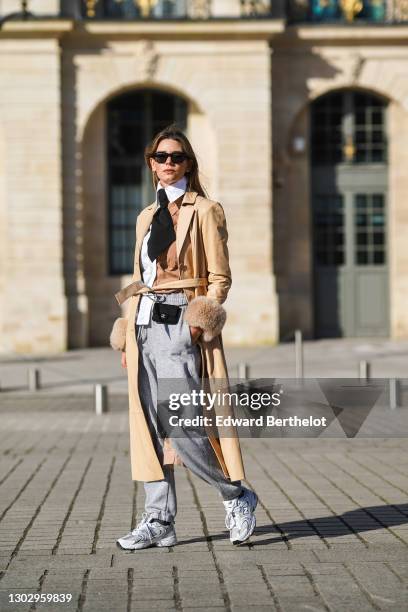 Natalia Verza wears sunglasses, a white and brown bi-color shirt, a black tie, a beige leather long trench coat with fluffy cuffs from Saks Potts, a...