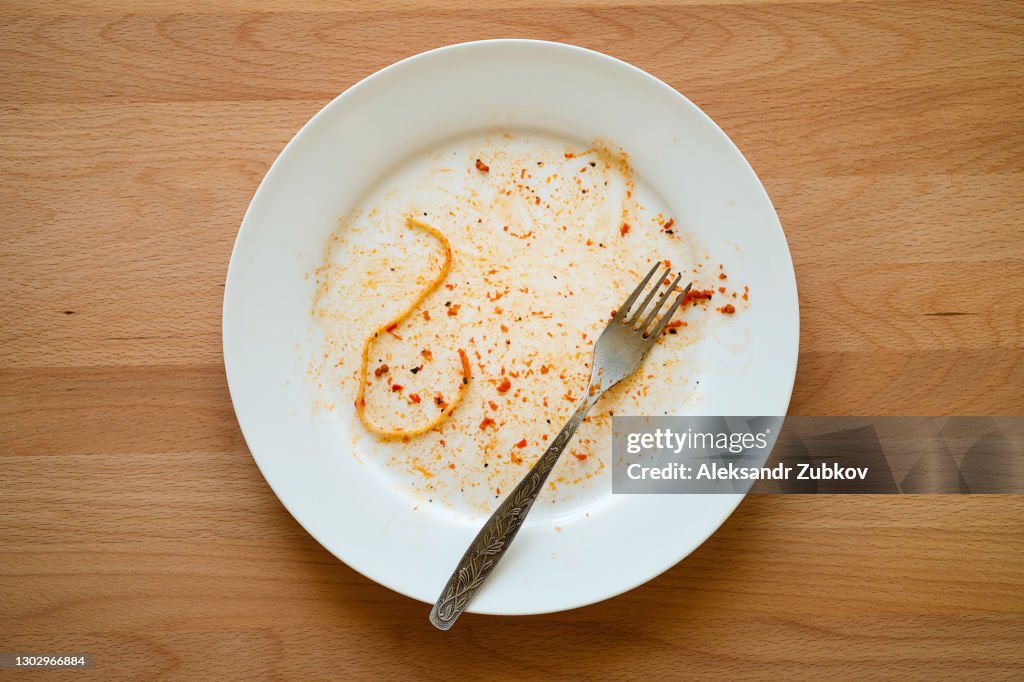 A dirty empty plate of pasta or spaghetti, a fork on a wooden table. Used cutlery, symbolize the end of lunch or dinner.