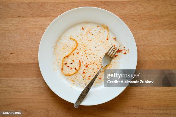 a dirty empty plate of pasta or spaghetti, a fork on a wooden table. used cutlery, symbolize the end of lunch or dinner. - dirty dish stock-fotos und bilder